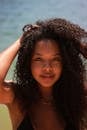 Close-up of a woman with curly hair enjoying a sunny day by the sea.